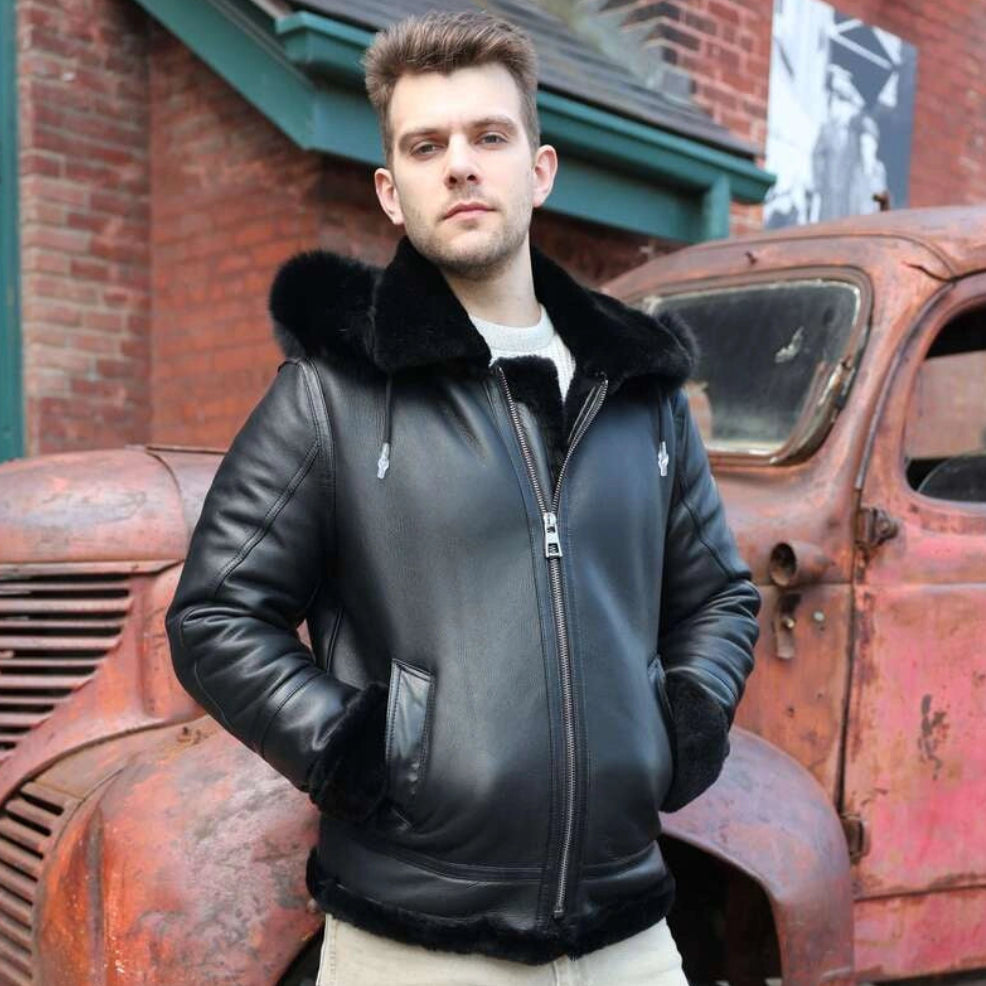 Man in a black leather jacket standing in front of an old rusted truck.