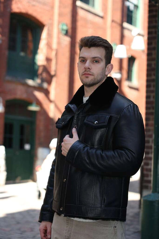 Man wearing a black leather jacket standing in an urban setting with brick buildings.