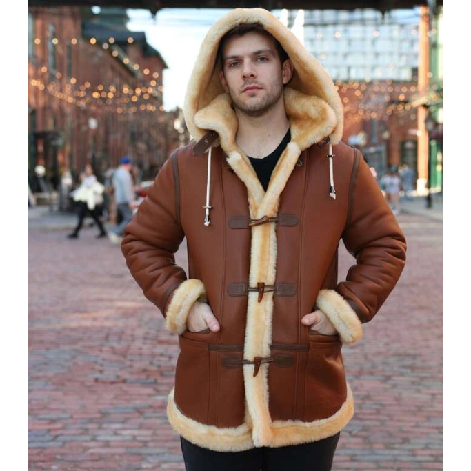 Person wearing a brown leather coat with fur trim in an urban setting.
