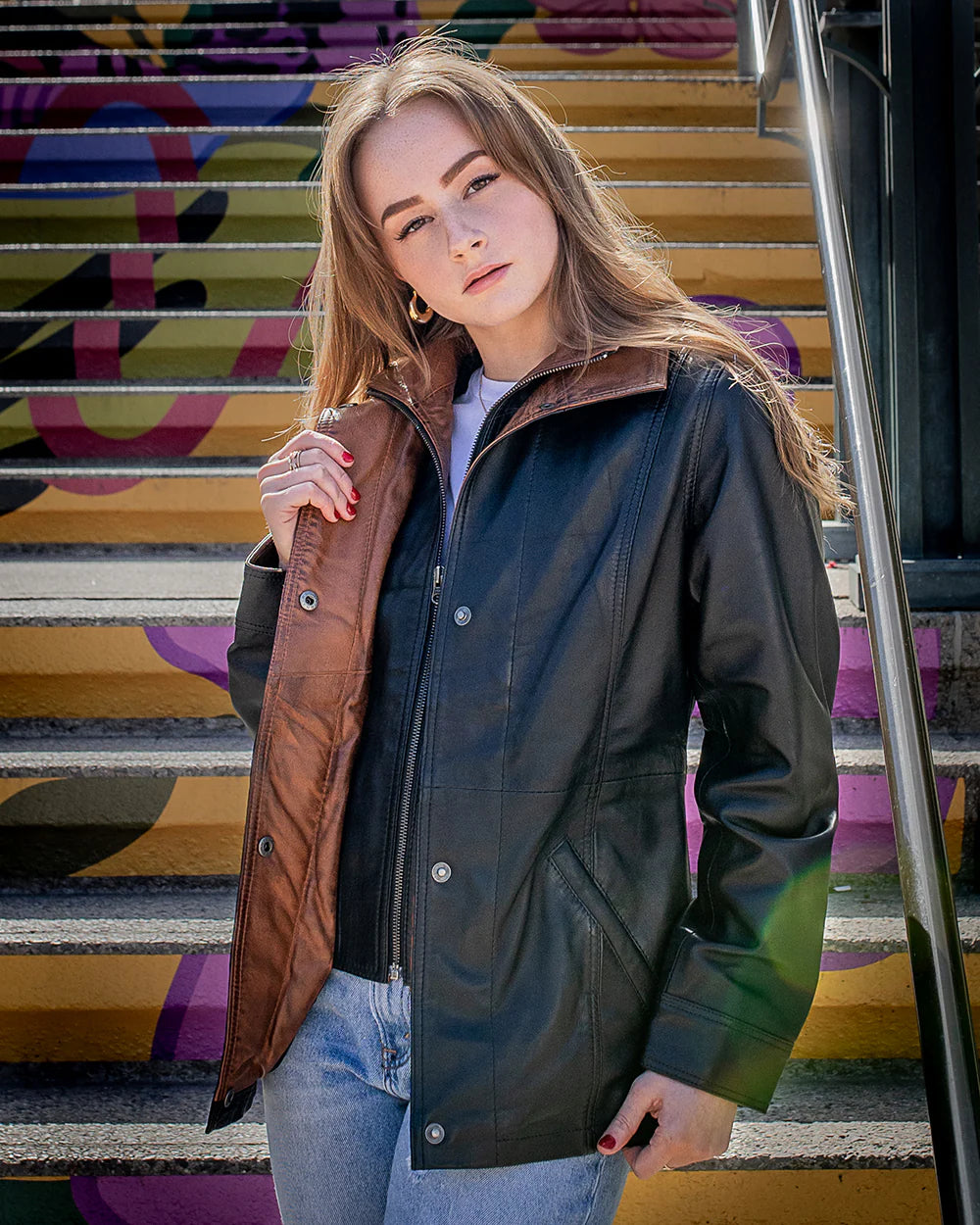 Lifestyle photoshoot of a woman wearing the Adeline black leather car coat, showcasing its elegant 3/4 length and regular fit on colorful steps.