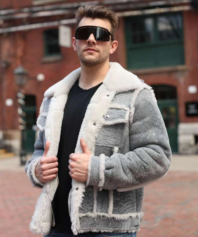 Man wearing a grey distressed shearling jacket with a brick building in the background.