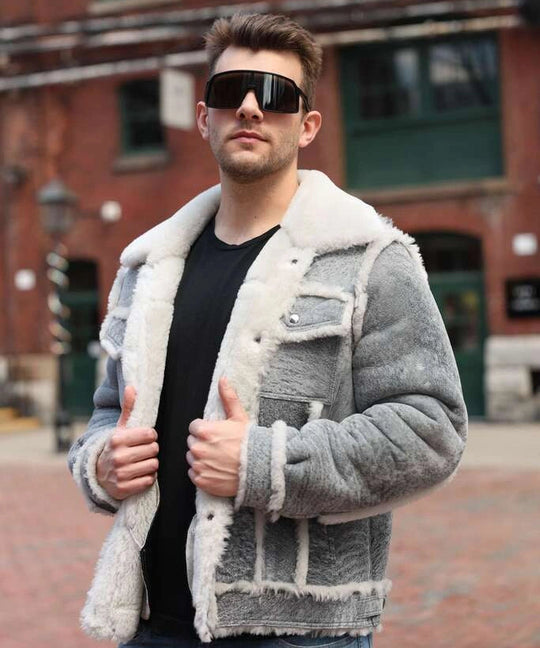 Man wearing a grey distressed shearling jacket with a brick building in the background.