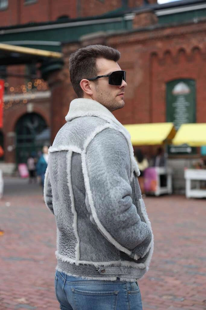 Man wearing a gray shearling jacket and sunglasses on a city street.