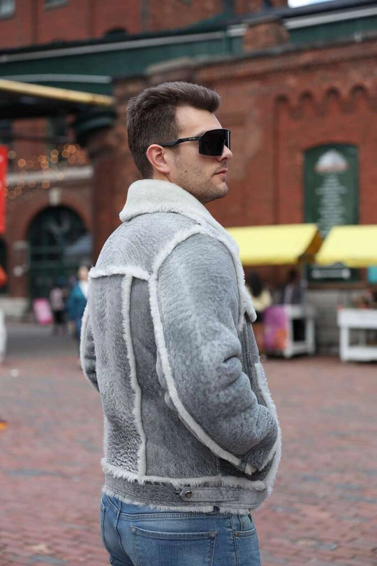 Man wearing a gray shearling jacket and sunglasses on a city street.