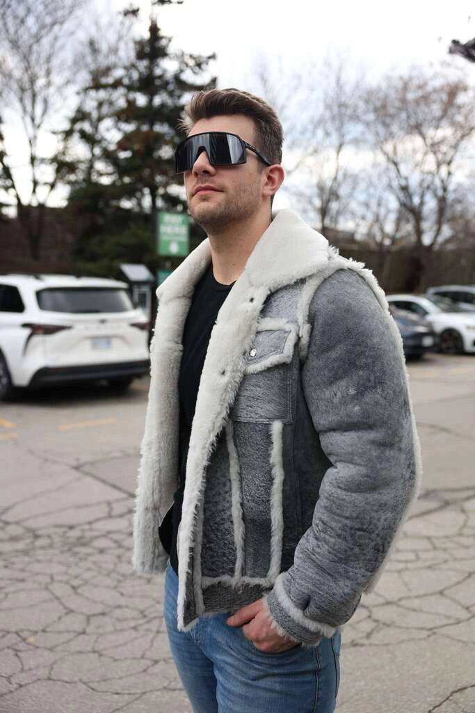 Man wearing a gray shearling jacket with white fur lining in an outdoor setting.