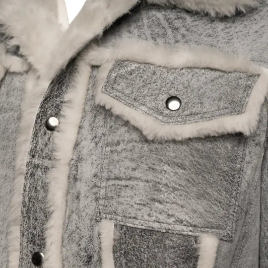 Close-up of Aiden's Grey Trucker Jacket showcasing the chest pocket with a snap button closure. The grey distressed fabric is complemented by the white shearling trim along the pocket and collar, adding a vintage touch.