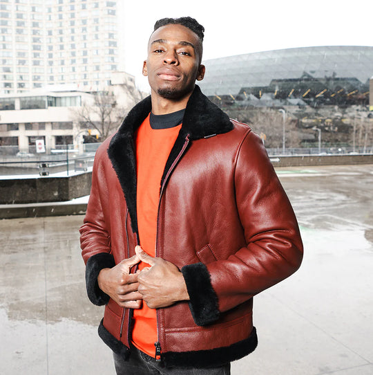 A man wearing the Aurelius Burgundy B3 Bomber Shearling Jacket over an orange shirt in an urban winter setting.