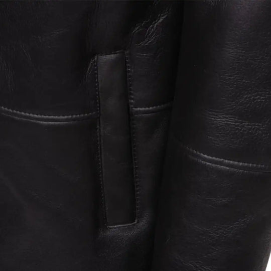 Close-up of a black shearling trench coat  pocket with stitching detail.