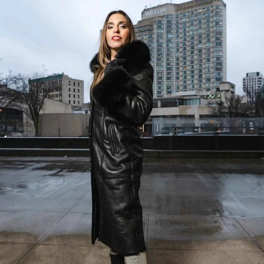 Woman in a black shearling sheepskin coat standing with cityscape in the background.