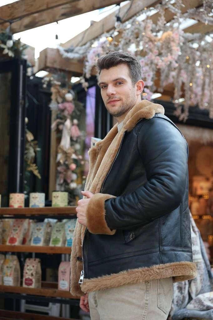 Man wearing Classic Ginger Brown B3 Bomber Aviator Shearling Jacket with brown fur trim in an indoor setting with decorative lights.
