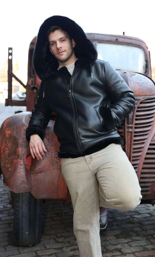 Person wearing Felix black bomber shearling jacket with fur hood leaning against an old, rusted truck.