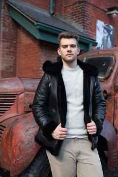 Man wearing Felix black bomber shearling jacket with fur collar standing next to an old red truck.