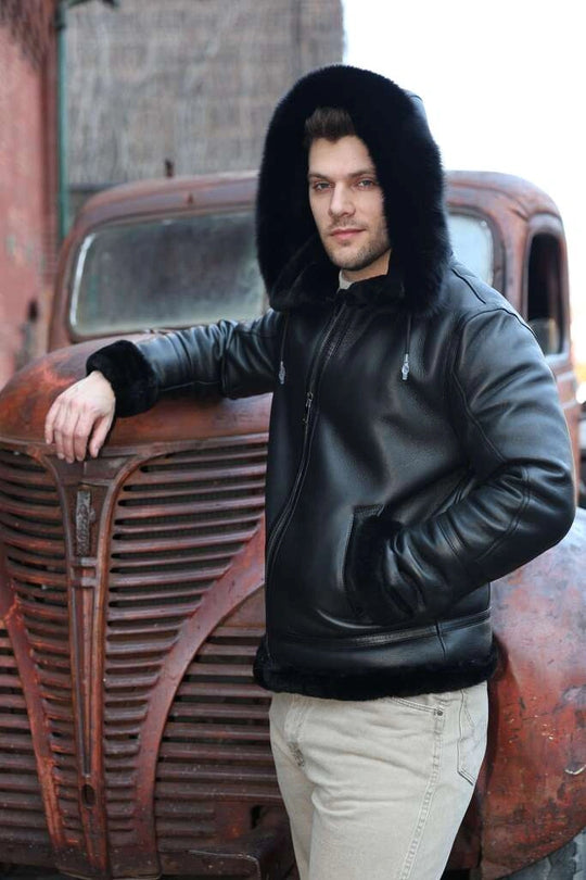 Man wearing Felix black bomber shearling jacket with fur hood leaning against an old rusted truck.