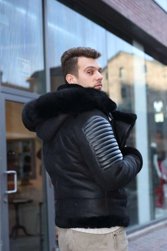 Man wearing Lucas Black Aviator Bomber Shearling Jacket with fur hood and ribbed sleeves in front of a glass building.