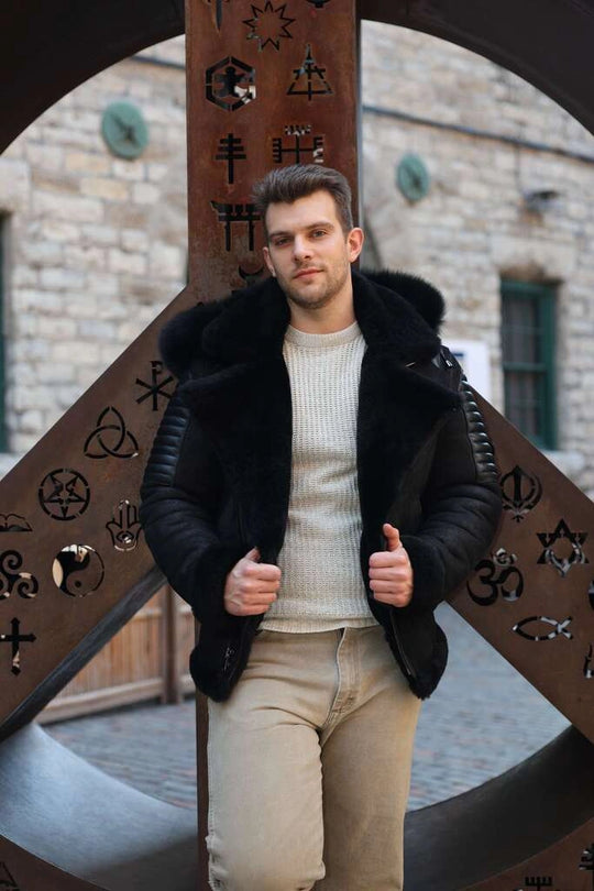 Man wearing Lucas Black Aviator Bomber Shearling Jacket with Hoodie , standing in front of a large decorative metal cross with intricate designs.