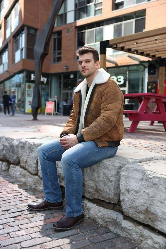 Man sitting on a stone bench wearing Lucian's distressed brown A2 Bomber shearling jacket in an urban setting.