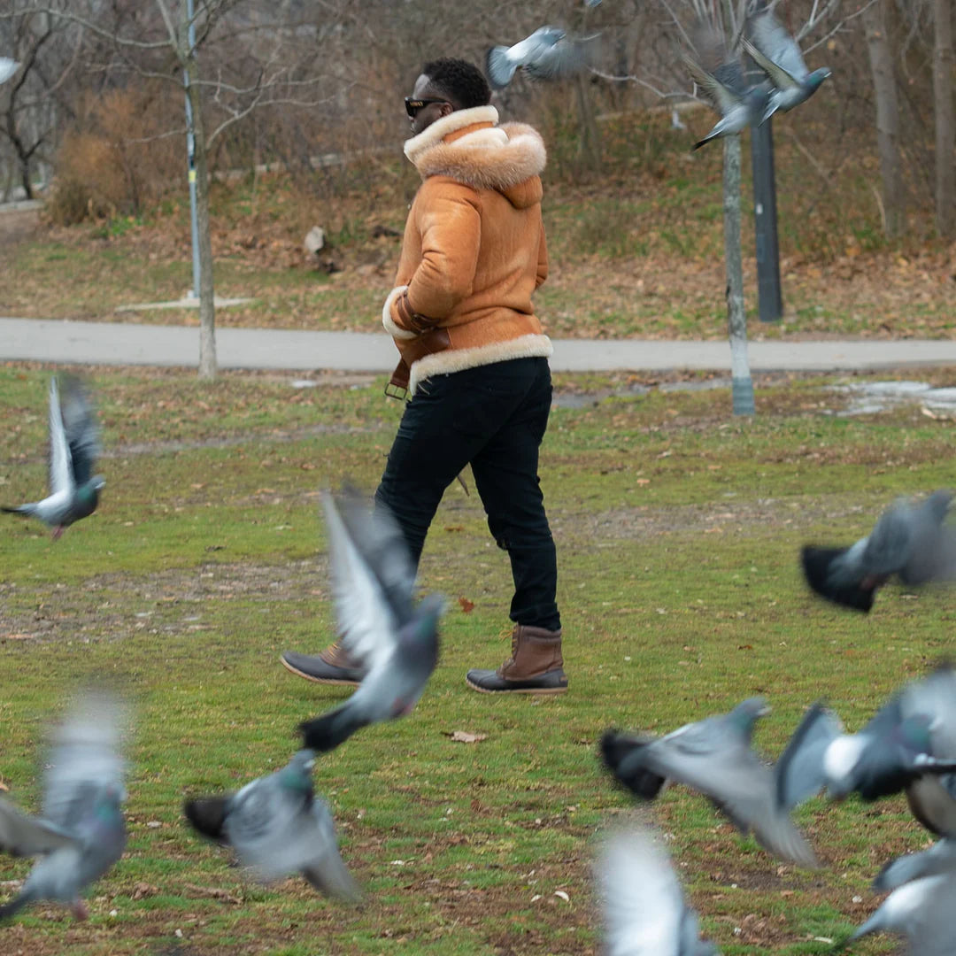 Person walking in a park wearing aviator shearling jacket with pigeons around in a winter setting.