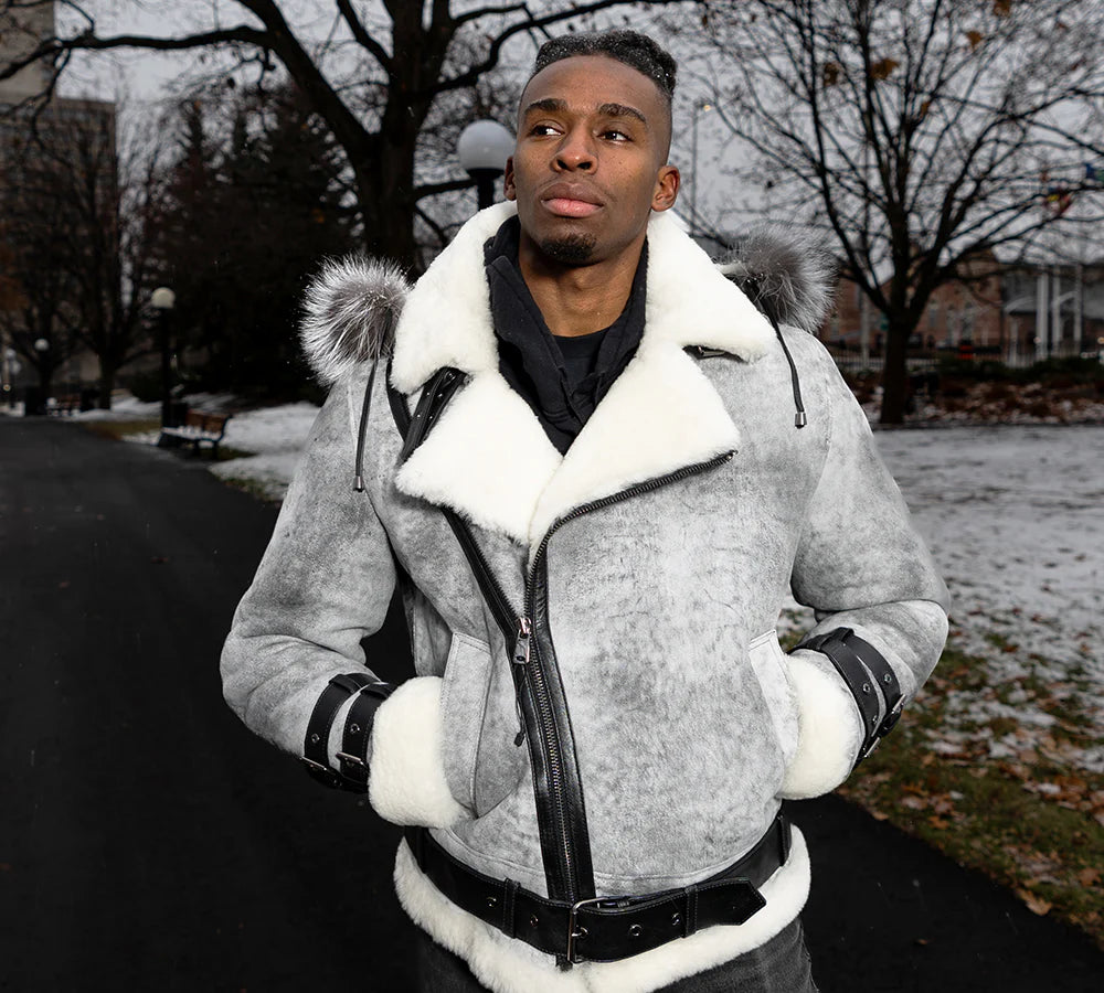 Man wearing a gray aviator shearling aviator bomber jacket with white fur trim outdoors on a snowy day.