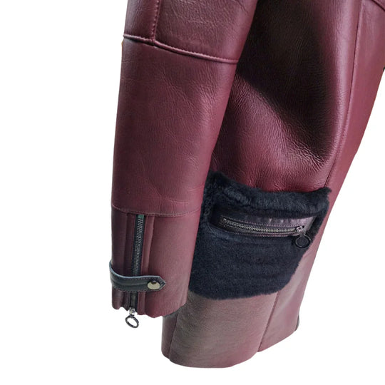 A close-up view of the sleeve on Samira's burgundy shearling coat, featuring a functional silver zipper at the cuff and a decorative black leather strap with a snap button.