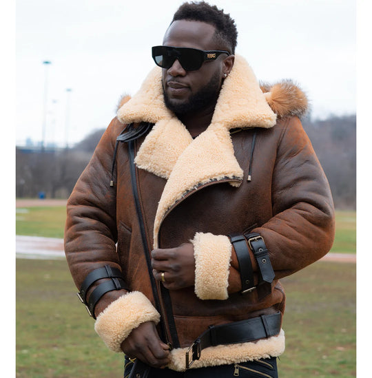 Lifestyle photoshoot of a man wearing Rocco vintage brown aviator shearling jacket featuring a classic cream shearling collar with a fur-lined hood in an outdoor setting. 